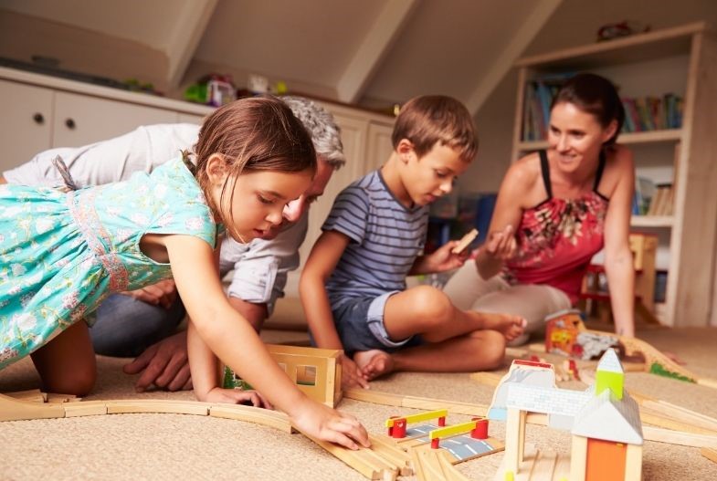 Parents playing on the floor building a wooden train track with their children